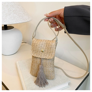 Détail de la pochette de téléphone en paille tressée avec pompon gris et boucle dorée