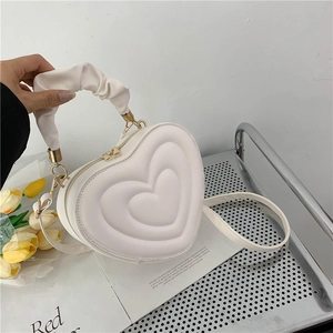 Detailed view of a white heart-shaped PU leather bag with quilted texture on a metal cart