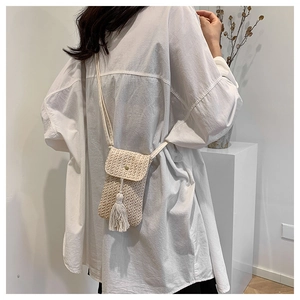 Petit sac bandoulière en paille pour téléphone avec pompon et fermoir porté par un mannequin