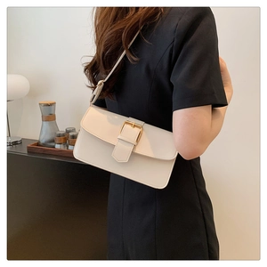 Detail of a minimalist cream-white shoulder bag with a gold buckle worn by a model