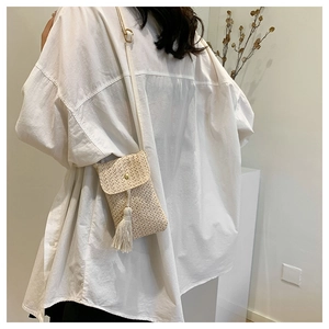 Sac bandoulière vertical en paille tressée avec pompon et bouton pression sur un mannequin