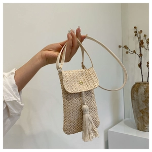 Détail du petit sac de téléphone en paille tressée avec pompon décoratif et bouton-pression