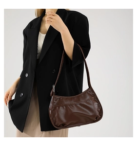 Close-up of brown crescent underarm bag with pleated texture and leather strap on shoulder