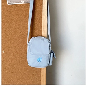 Detail der hellblauen Umhängetasche mit gesticktem Logo und kleinem Zubehörbeutel
