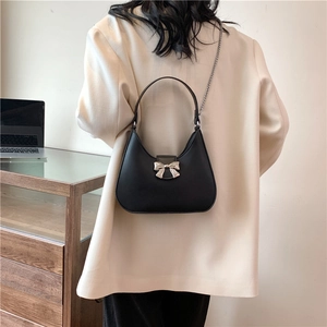 Women's black leather half-moon bag with silver bow buckle and chain strap on shoulder