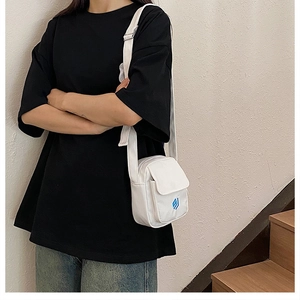 Detailansicht einer weißen Canvas-Umhängetasche mit Vordertasche und blauem Logo