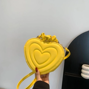 Detail of yellow heart-shaped PU leather bag with ruffle handle and embossed pattern