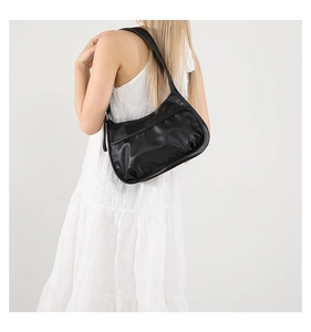 Black crescent underarm bag with pleated design worn on shoulder by a model in white dress
