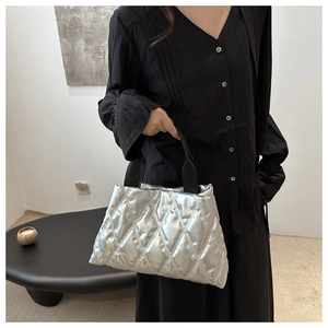 Macro detail of metallic silver quilted bucket bag with black strap held by model