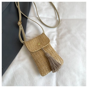 Détail de la pochette de téléphone en paille tressée avec pompon et fine bandoulière