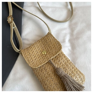 Détail du sac de téléphone en paille tressée avec fermoir doré et pompon décoratif