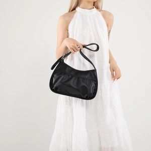 Minimalist black crescent shoulder bag in matte PU leather worn by a model in white dress