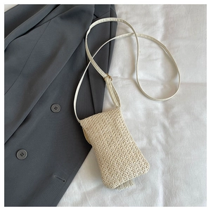 Détail d'un sac bandoulière en paille blanc cassé avec des glands et une fine lanière