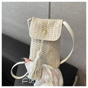 Détail d'un sac à téléphone en paille tressée crème avec un pompon et un fermoir doré
