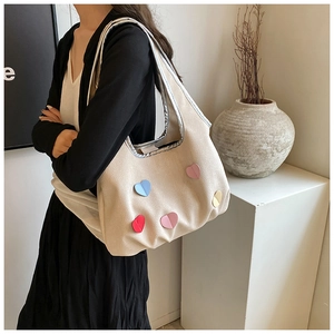 Detail of cream knit tote bag with colorful heart patches and silver metallic handles