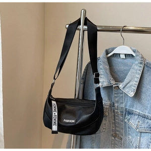 Détail du sac bandoulière noir en cuir grainé avec sangles logo sur un support