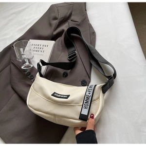 Détail d'un sac demi-lune en cuir grainé blanc cassé avec étiquette sur blazer marron