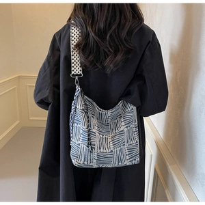 Detail view of large striped canvas crossbody bag with wide strap and tassel on black coat
