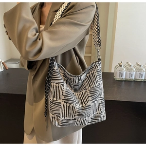 Detail of striped canvas tote with wide woven shoulder strap and tassel accessory on model