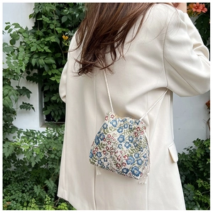 Detail of floral embroidery on a mini bucket bag with drawstring and white cord strap