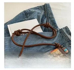 Detail of colorful woven straw crossbody bag with brown leather cord strap and knotted trim