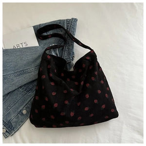 Détail d'un sac cabas en velours côtelé noir avec motif fraise rouge et large bandoulière