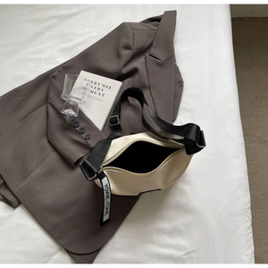Détail du sac dumpling crème en cuir texturé avec bandoulière marquée HOMME+FEMME