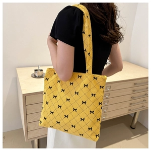 Détail du sac cabas en velours jaune avec motifs de nœuds noirs et coutures matelassées
