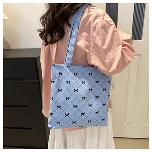 Détail du sac cabas en velours côtelé bleu clair à motifs de nœuds porté à l'épaule