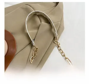 Détail de la bandoulière en cuir blanc avec chaîne dorée sur un sac demi-lune beige