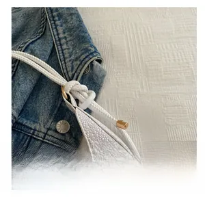 Close-up of white embossed leather handbag featuring knot details and golden hardware