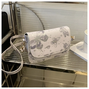 Detail of white shoulder bag with purple butterfly print and golden hardware on a glass shelf