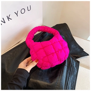 Close-up of vibrant magenta quilted puffer bag on black leather texture and white backdrop