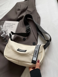 Sac bandoulière beige demi-lune avec étiquette mode et sangle sur blazer marron