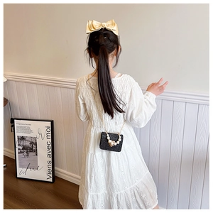 Petite fille portant une robe brodée blanche et un sac à main à paillettes avec perles