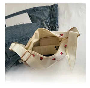 Vue détaillée intérieure d'un sac bandoulière en toile blanche avec broderie fraise