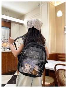 Detail of a black ita-bag backpack with a clear PVC window showing plush dolls at a cafe