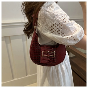 Close-up of wine red faux crocodile skin texture and gold metal buckle on a half-moon bag