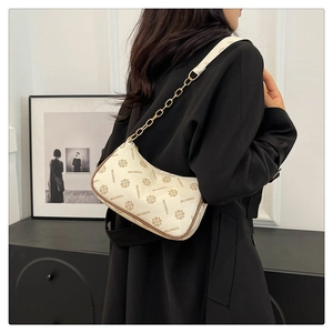 Détail du sac demi-lune crème avec motif monogramme et bandoulière en chaîne dorée