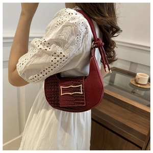 Detail of burgundy crocodile-embossed crescent bag with gold buckle and knotted strap