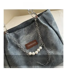 Dettaglio della borsa in denim lavato con catena d'argento e ciondoli con perle grandi