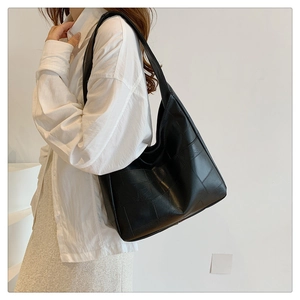 Detail view of large black tote bag with square lattice texture on a female model