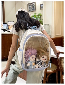 Detail view of cream ita bag featuring a large clear PVC window and plush dolls inside