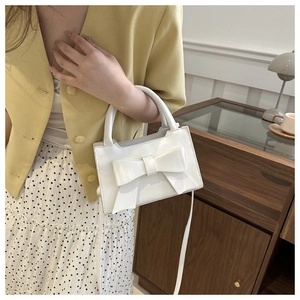 Elegant white glossy leather handbag featuring a large bow detail in a French cafe setting