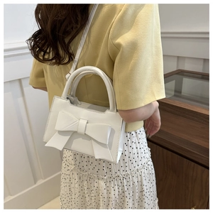 Close-up of white crossbody bag with large bow detail and cylindrical top handle