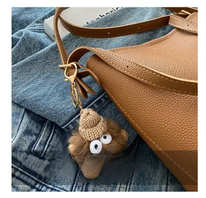 Gros plan d'une breloque monstre en peluche marron avec un bonnet en tricot sur un sac en cuir