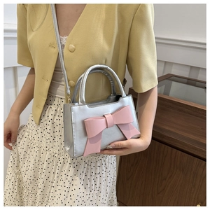 Detailed view of silver metallic handbag featuring a large pink bow and thin shoulder strap