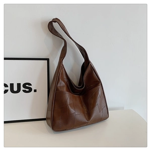 Detail of a brown leather patchwork hobo bag with textured geometric panels and a wide strap