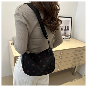 Détail d'un sac bandoulière noir en forme de lune avec imprimé fraises rouges