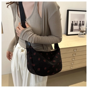 Gros plan d'un sac selle en velours noir avec broderie fraise et large bandoulière